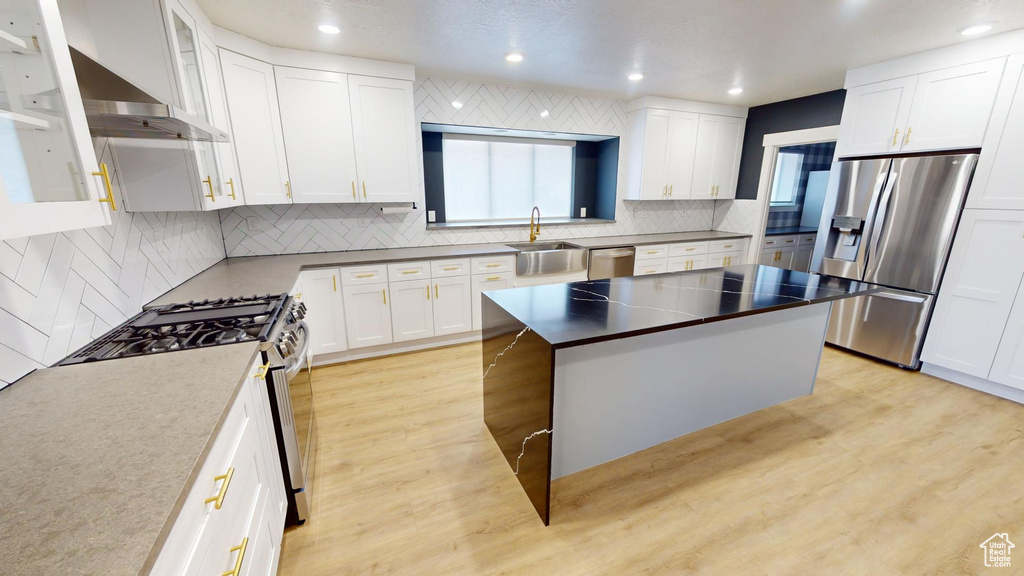 Kitchen with a kitchen island, white cabinetry, sink, stainless steel appliances, and light wood-type flooring