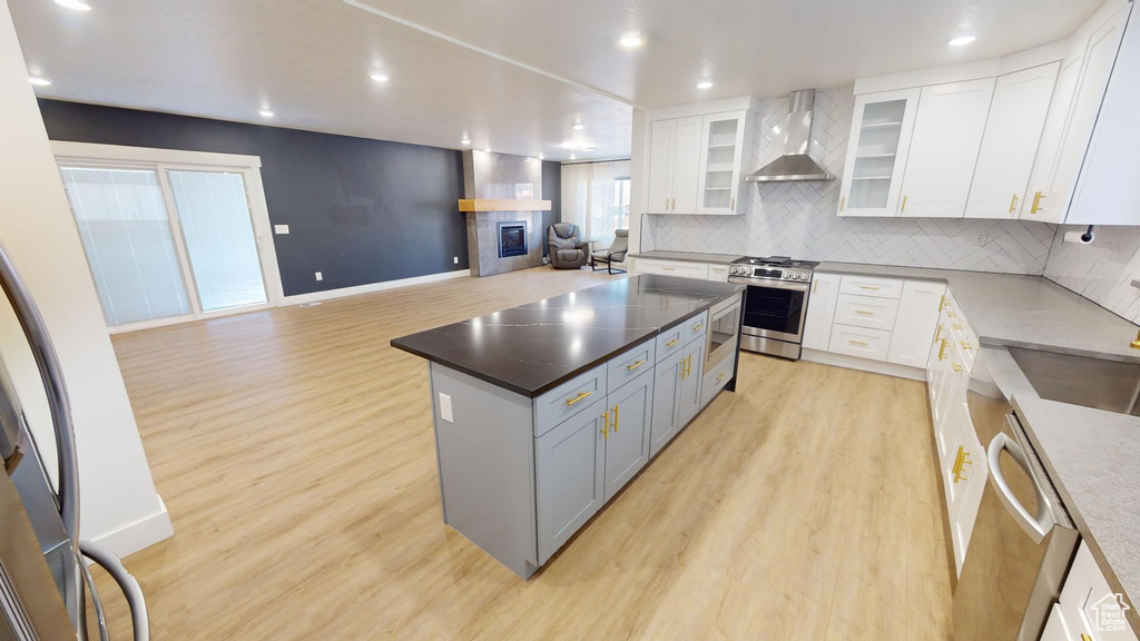 Kitchen featuring a center island, light hardwood / wood-style flooring, white cabinets, stainless steel appliances, and wall chimney range hood
