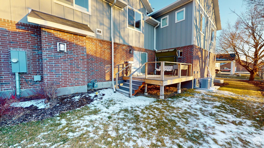 Snow covered back of property featuring a deck and central air condition unit