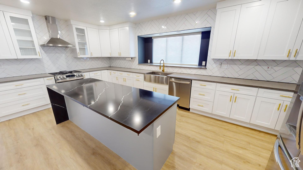 Kitchen with white cabinets, stainless steel appliances, light hardwood / wood-style floors, and wall chimney exhaust hood