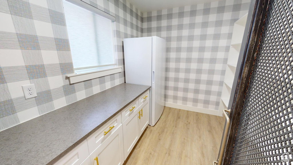 Kitchen with white cabinetry, white refrigerator, and light hardwood / wood-style flooring