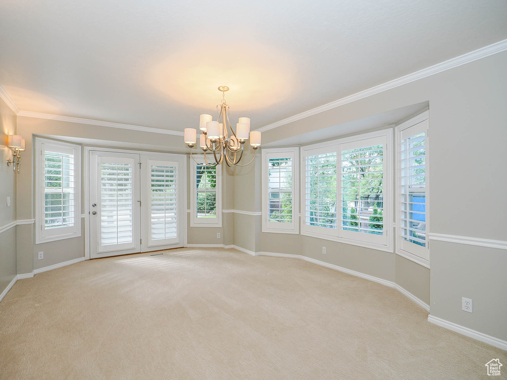 Carpeted spare room with ornamental molding and a chandelier