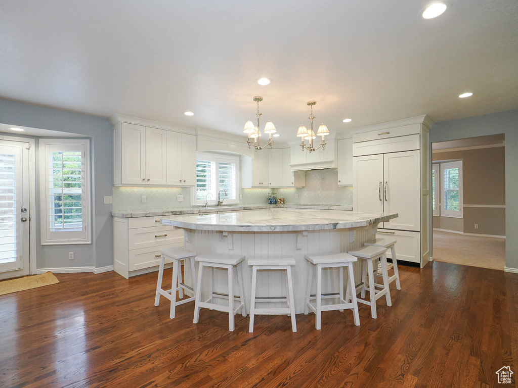 Kitchen featuring a large island, light stone counters, white cabinetry, and dark wood-type flooring
