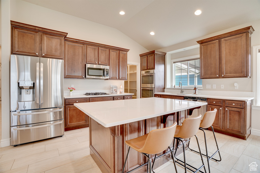 Kitchen featuring light countertops, lofted ceiling, a kitchen island, and stainless steel appliances