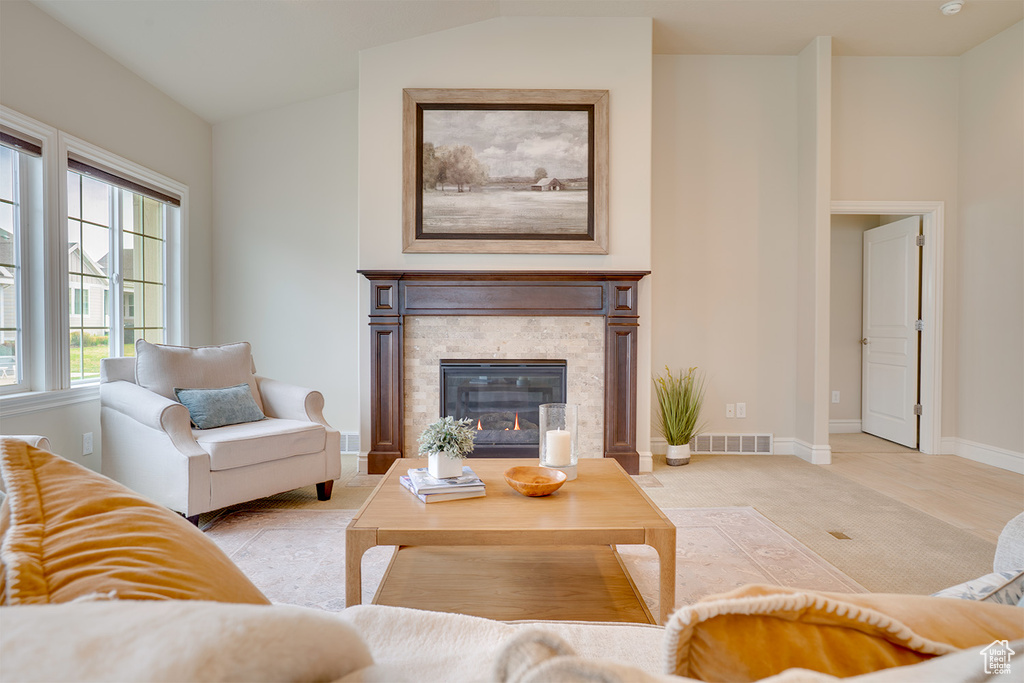 Living area with vaulted ceiling, a stone fireplace, light carpet, baseboards, and visible vents