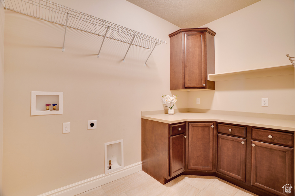 Washroom with electric dryer hookup, light tile patterned floors, cabinet space, baseboards, and washer hookup