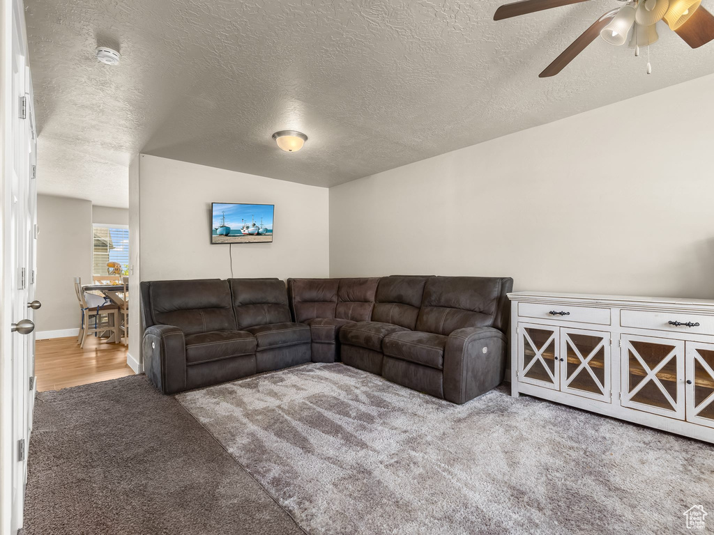 Carpeted living room with ceiling fan, a textured ceiling, and lofted ceiling