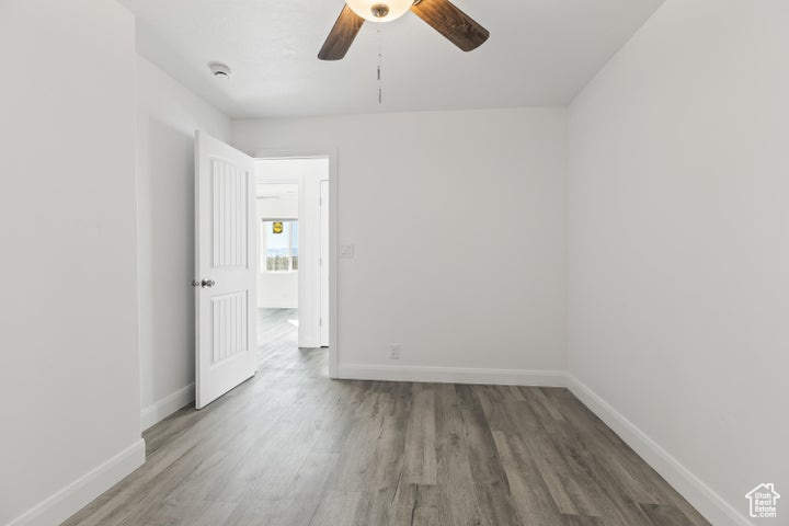 Empty room featuring wood finished floors, baseboards, ceiling fan, and a smoke detector