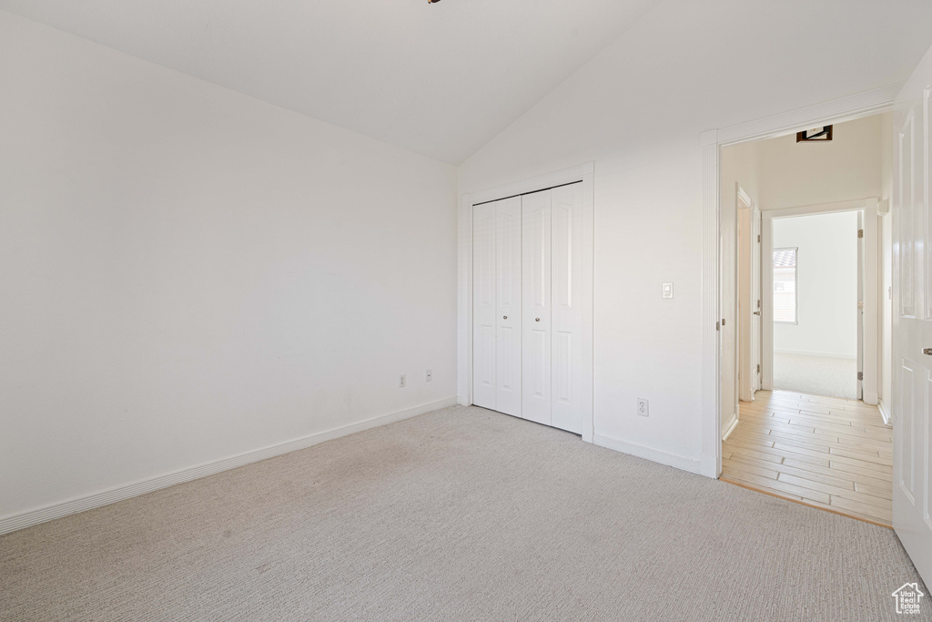 Unfurnished bedroom featuring high vaulted ceiling, light colored carpet, and a closet