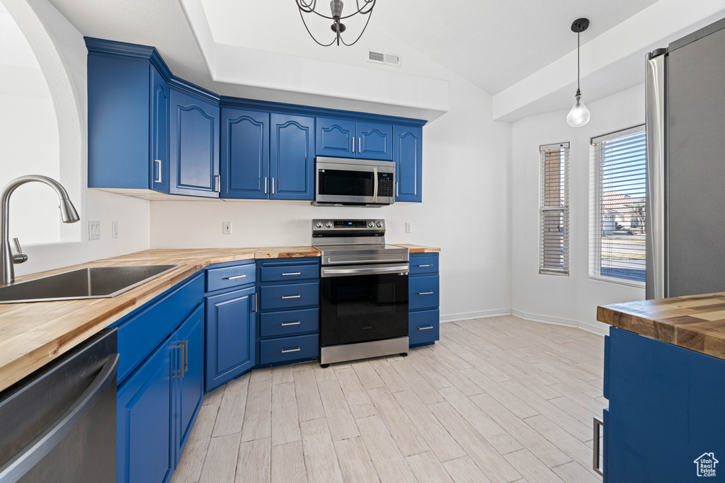 Kitchen featuring appliances with stainless steel finishes, pendant lighting, blue cabinets, butcher block counters, and sink