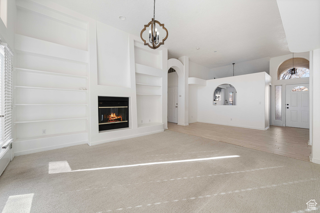 Unfurnished living room featuring light carpet, an inviting chandelier, and built in shelves