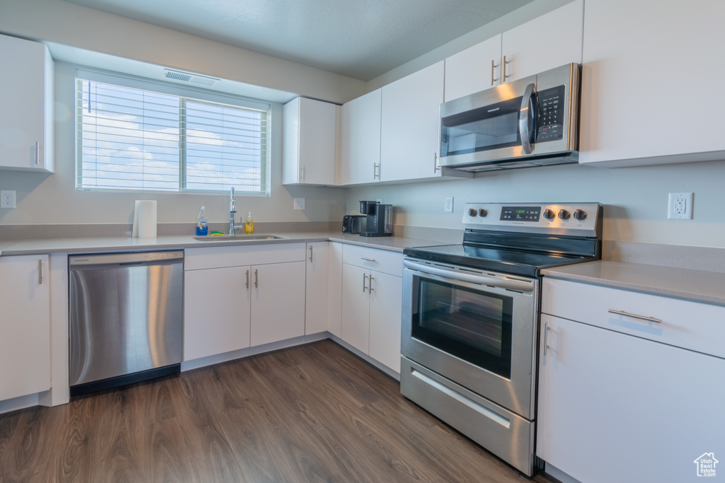 Kitchen featuring appliances with stainless steel finishes, a sink, dark wood finished floors, white cabinets, and light countertops