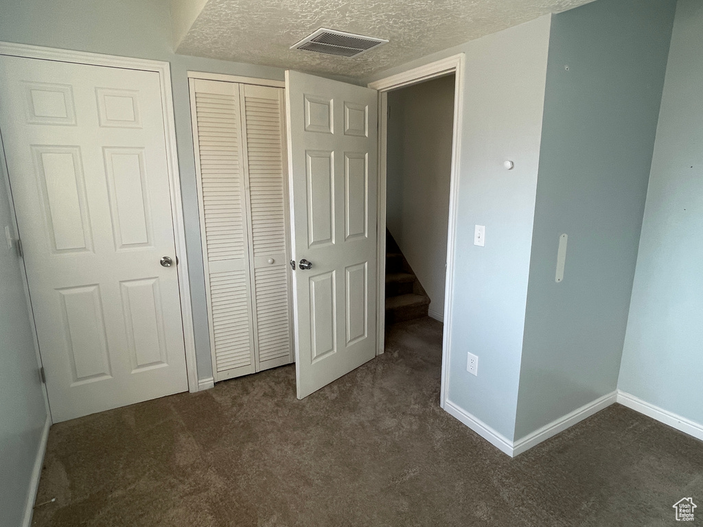 Unfurnished bedroom featuring dark carpet, a closet, and a textured ceiling