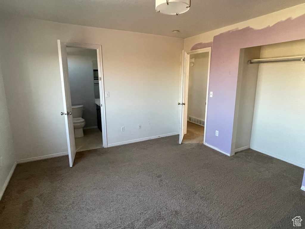Unfurnished bedroom featuring ensuite bathroom and dark carpet
