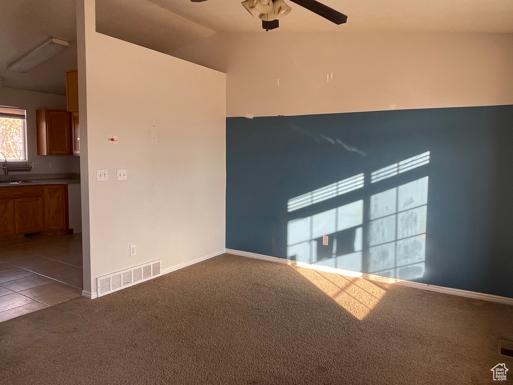 Carpeted spare room featuring ceiling fan, lofted ceiling, and sink