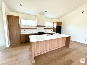 Kitchen with lofted ceiling, sink, black refrigerator, a center island, and light wood-type flooring