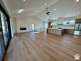 Unfurnished living room featuring lofted ceiling, a fireplace, ceiling fan, and light wood-type flooring