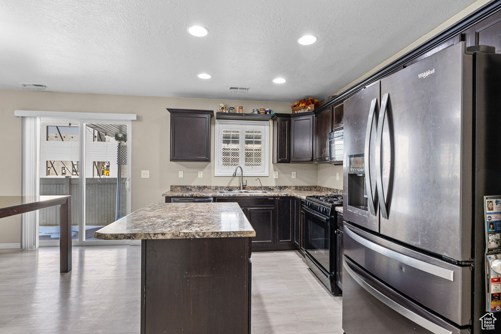 Kitchen with a kitchen island, sink, black appliances, dark brown cabinets, and a textured ceiling