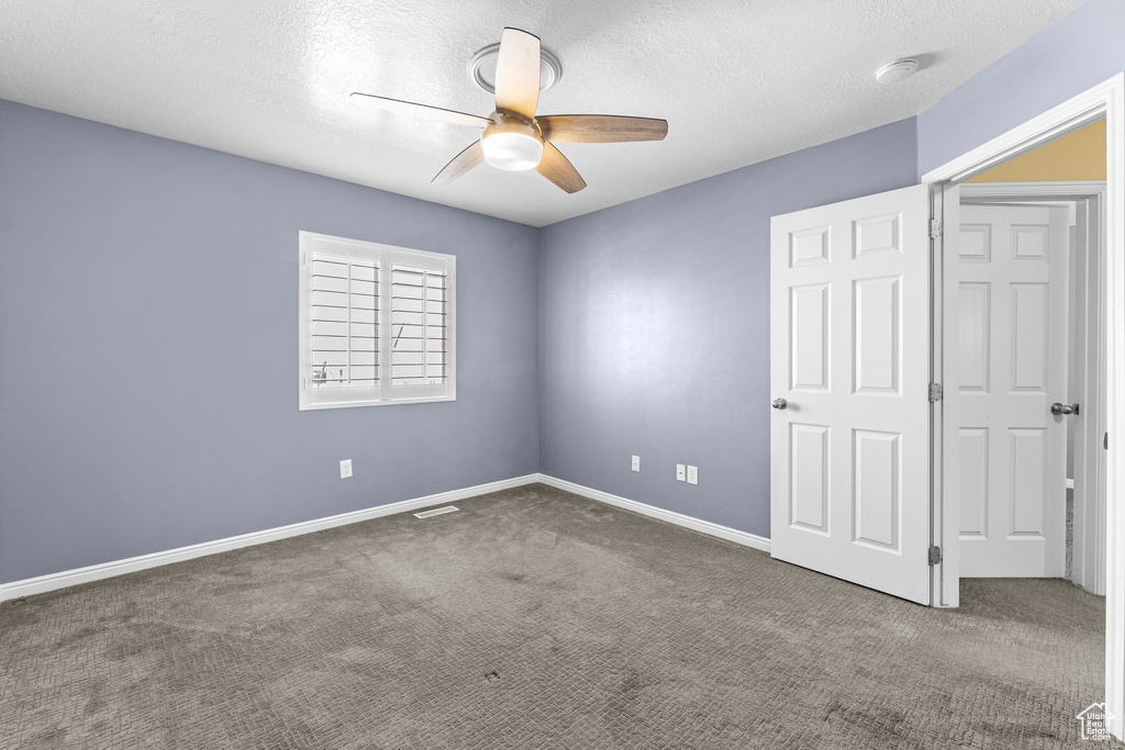 Unfurnished bedroom with ceiling fan, dark carpet, and a textured ceiling