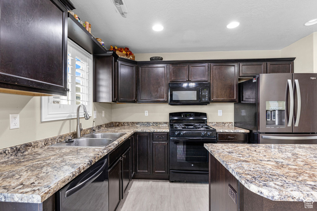 Kitchen featuring sink, dark brown cabinetry, black appliances, light stone countertops, and a textured ceiling