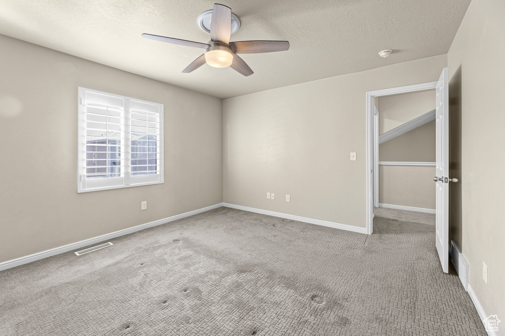 Spare room with ceiling fan, light colored carpet, and a textured ceiling