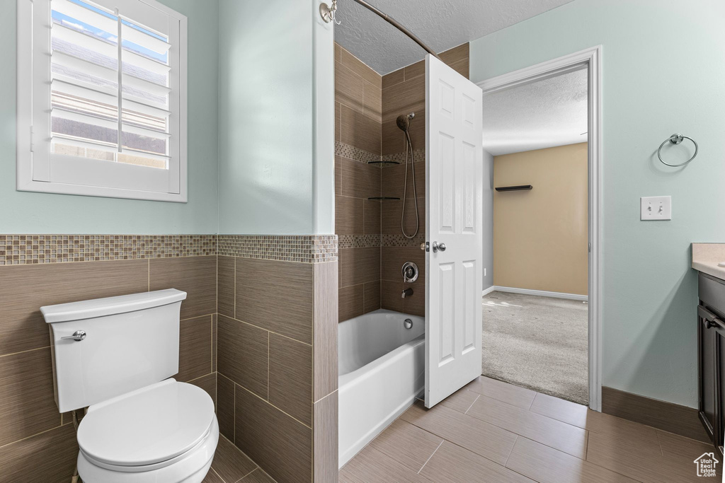 Full bathroom with tiled shower / bath, tile walls, vanity, toilet, and a textured ceiling