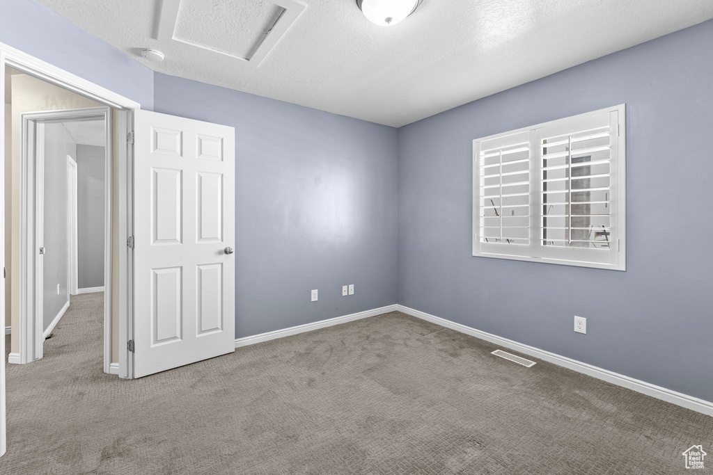 Empty room with light colored carpet and a textured ceiling