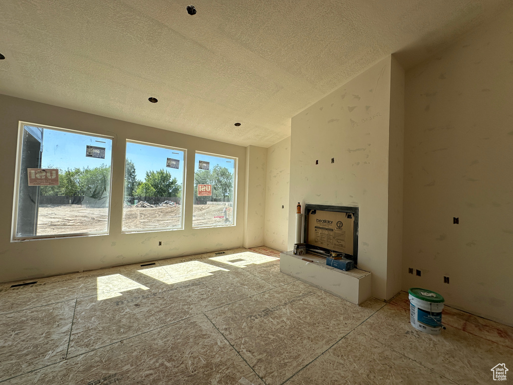 Unfurnished living room featuring a textured ceiling and vaulted ceiling