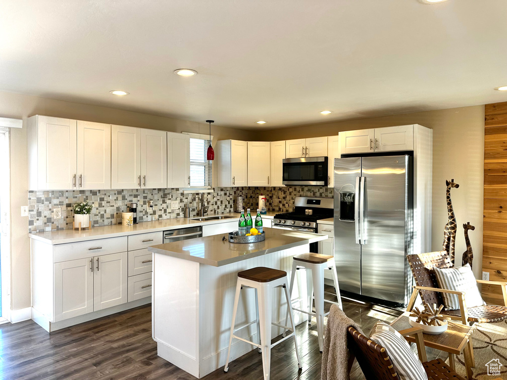 Kitchen featuring a kitchen bar, white cabinetry, decorative light fixtures, a center island, and stainless steel appliances