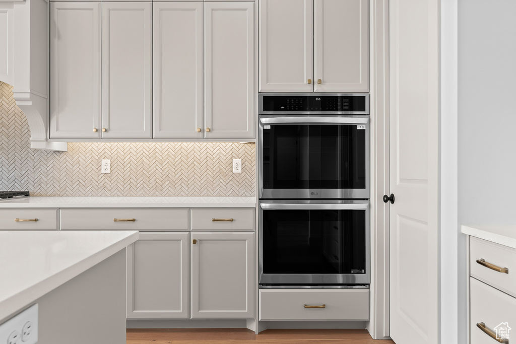 Kitchen featuring white cabinetry, stainless steel double oven, and decorative backsplash