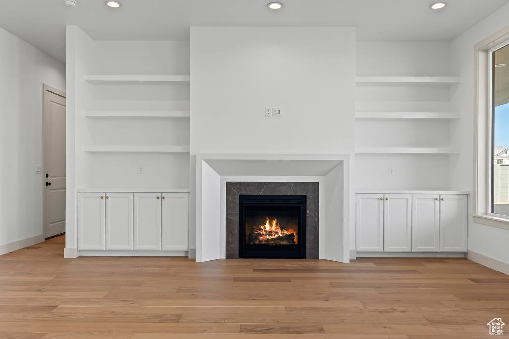 Unfurnished living room featuring built in shelves and light hardwood / wood-style flooring