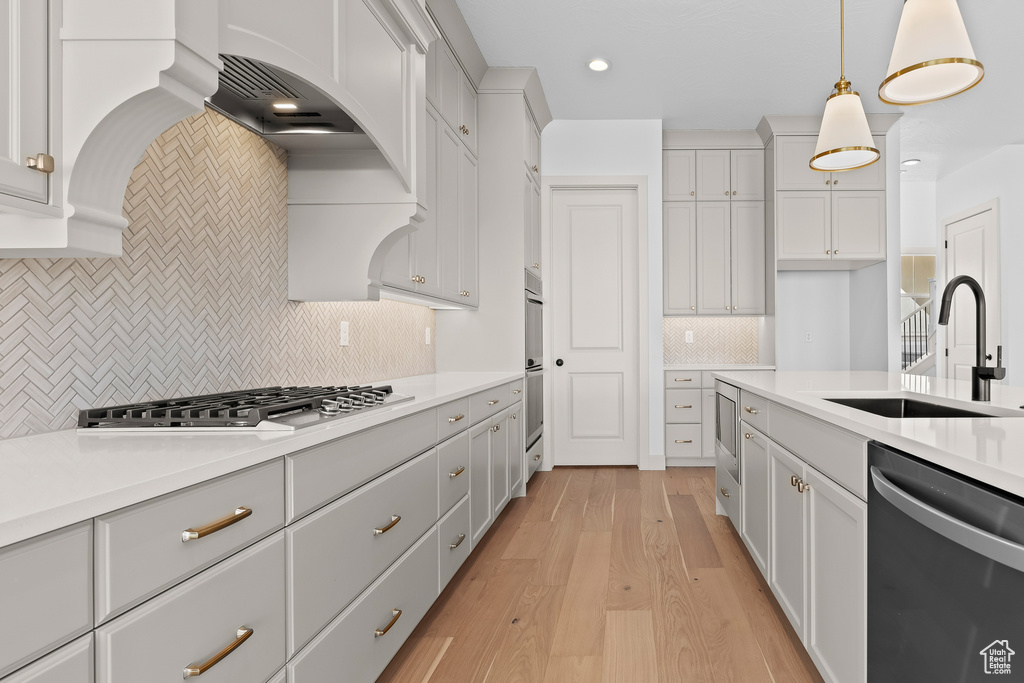 Kitchen featuring sink, dishwasher, hanging light fixtures, stainless steel gas cooktop, and light wood-type flooring