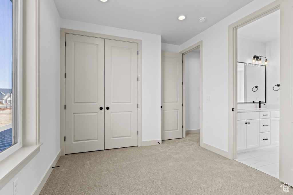 Unfurnished bedroom featuring connected bathroom, sink, light colored carpet, and a closet