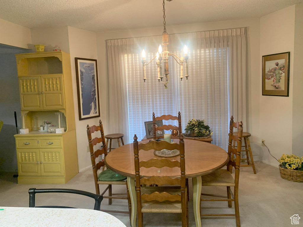 Dining area with light carpet, a textured ceiling, and an inviting chandelier