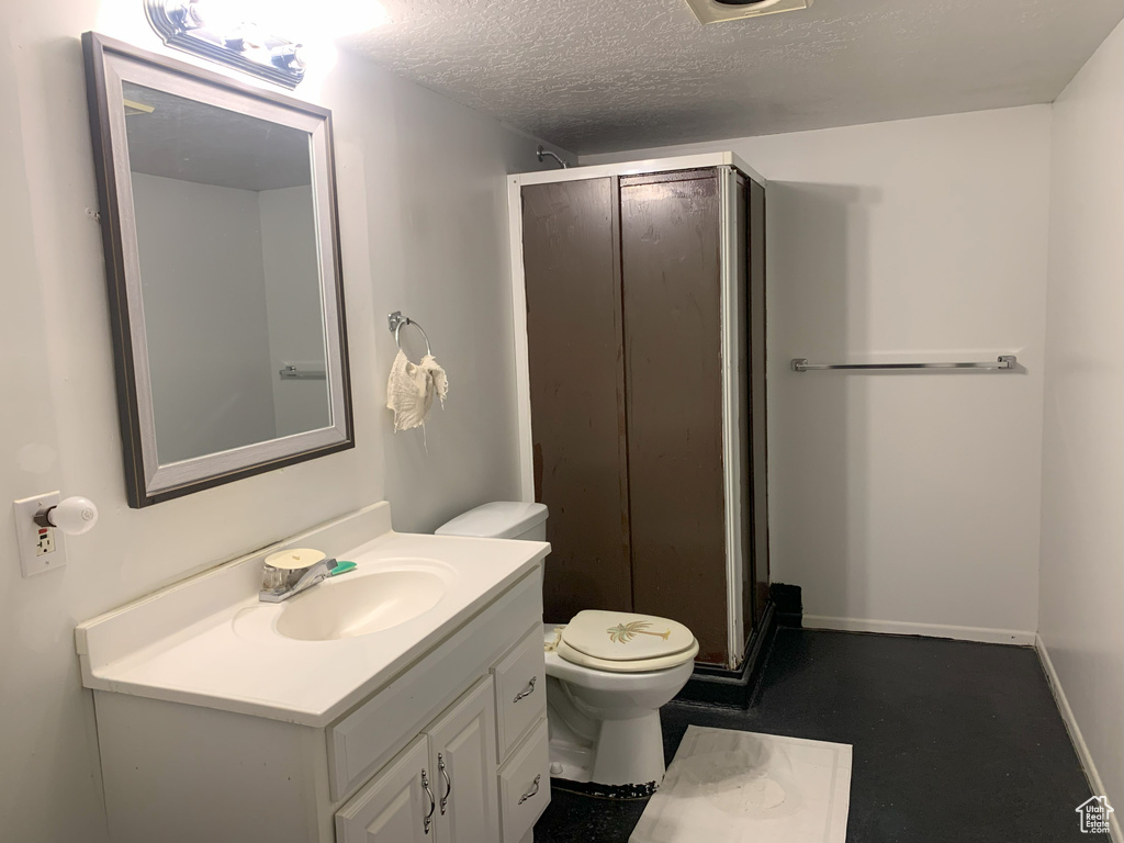 Bathroom featuring vanity, toilet, a textured ceiling, and walk in shower
