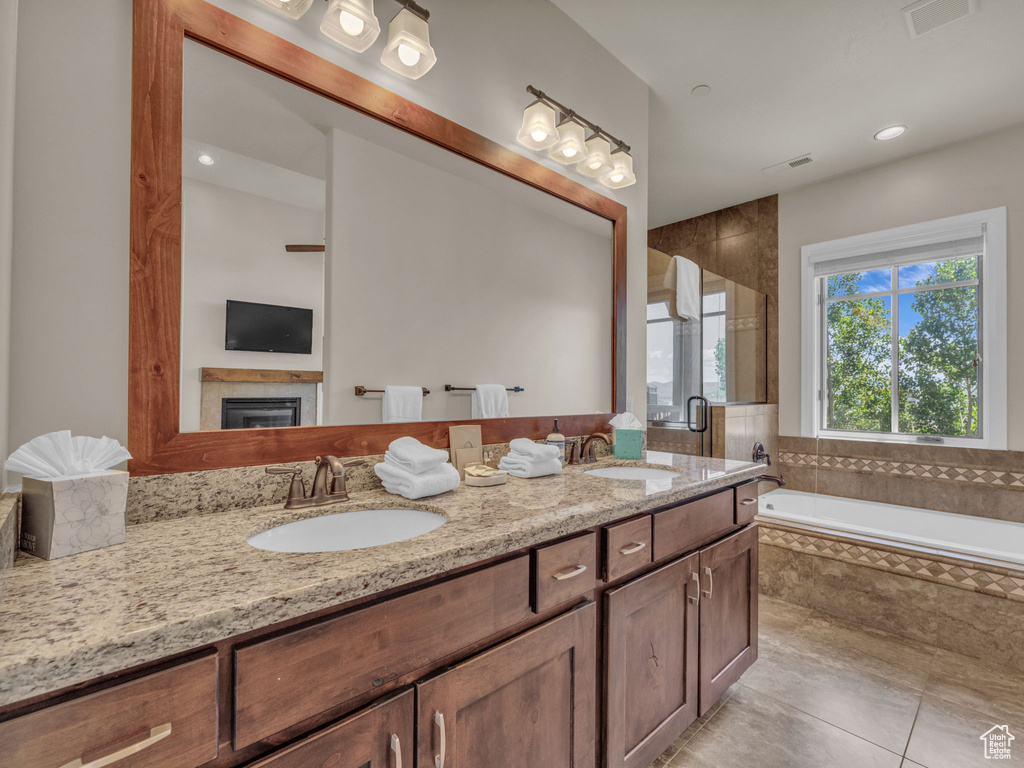 Full bathroom with double vanity, a garden tub, a stall shower, tile patterned floors, and a glass covered fireplace
