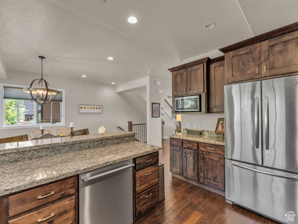Kitchen with appliances with stainless steel finishes, dark wood-style floors, light stone counters, a chandelier, and recessed lighting