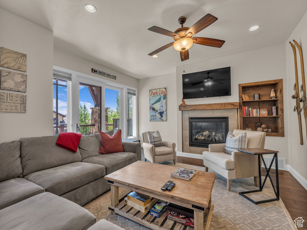 Living room with wood finished floors, a ceiling fan, baseboards, a tile fireplace, and recessed lighting