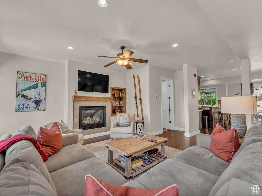 Living room with wood finished floors, a tiled fireplace, recessed lighting, baseboards, and a ceiling fan