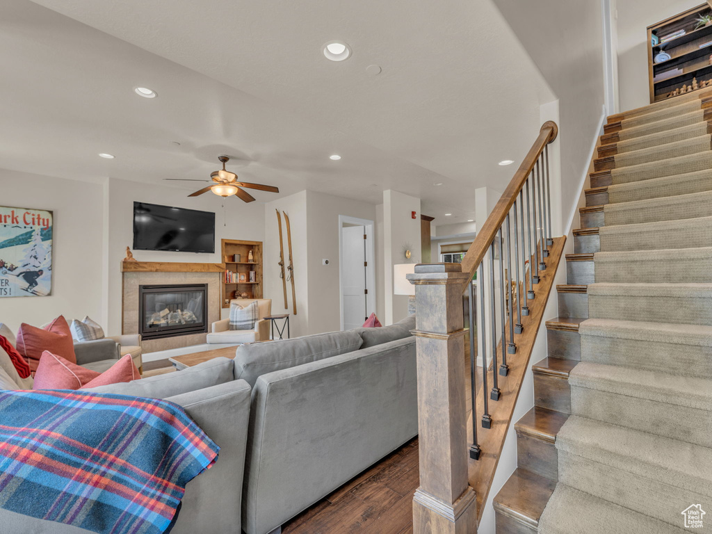 Living area with recessed lighting, dark wood-style flooring, stairs, a glass covered fireplace, and ceiling fan