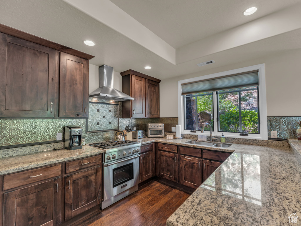 Kitchen with stainless steel range, a sink, wall chimney range hood, light stone countertops, and decorative backsplash