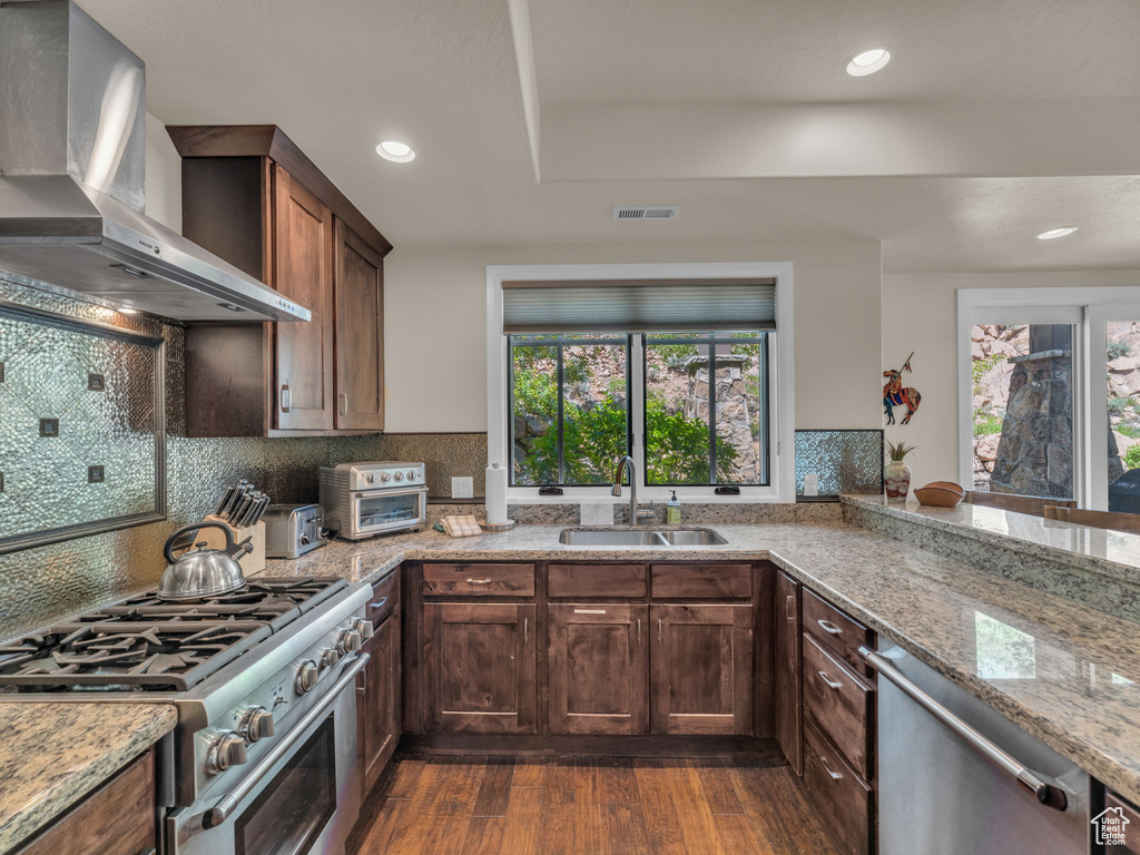 Kitchen with wall chimney exhaust hood, a sink, stainless steel appliances, dark wood-style floors, and light stone countertops