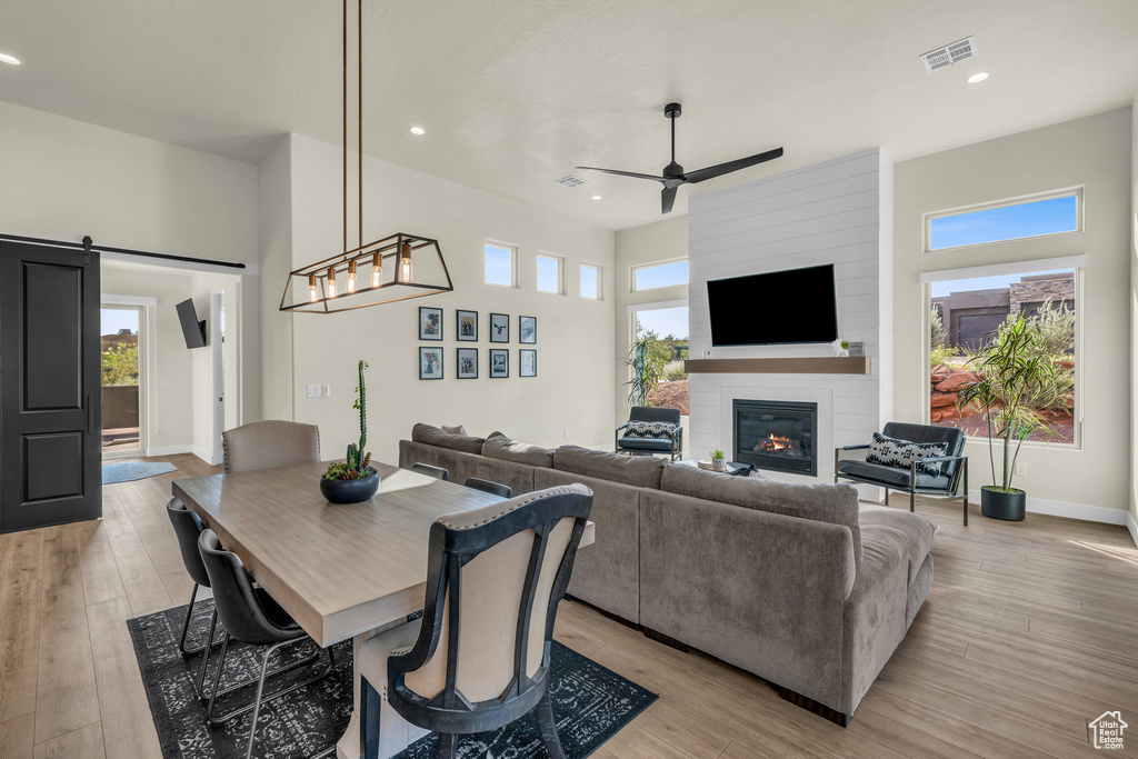 Dining room featuring a fireplace, a barn door, ceiling fan, and light wood-type flooring