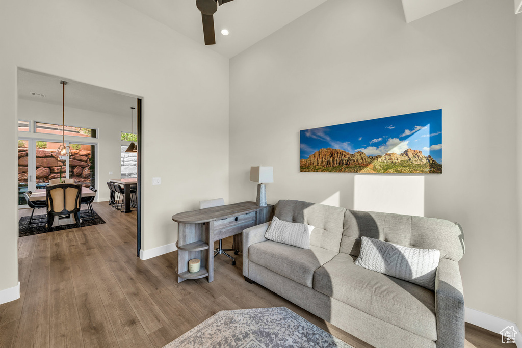Living room with hardwood / wood-style flooring, a towering ceiling, and ceiling fan with notable chandelier
