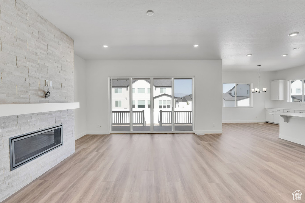 Unfurnished living room with a stone fireplace, light wood-type flooring, recessed lighting, and a chandelier