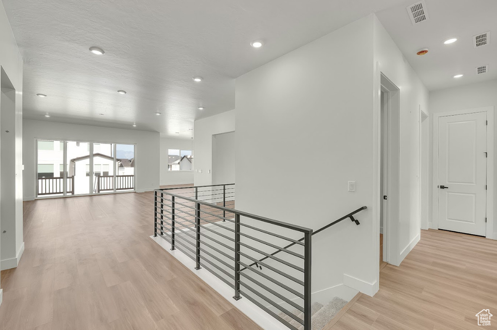 Corridor with an upstairs landing, light wood finished floors, and recessed lighting