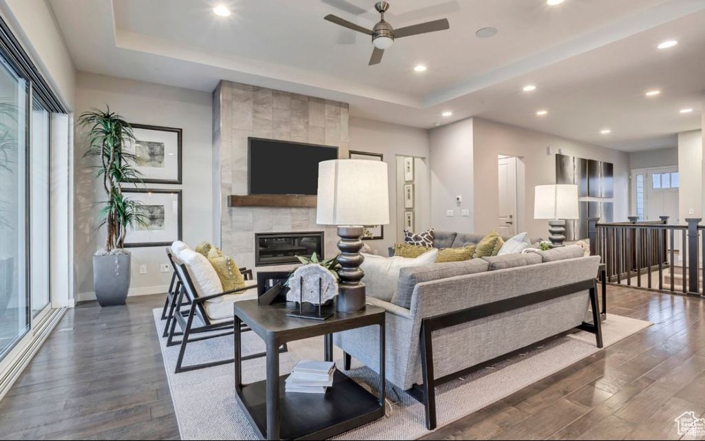 Living room with a raised ceiling, a tile fireplace, dark hardwood / wood-style floors, and ceiling fan