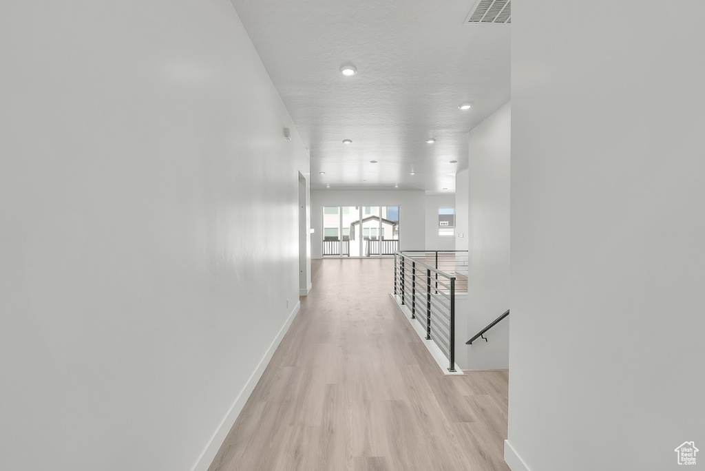 Corridor with an upstairs landing, light wood finished floors, and recessed lighting