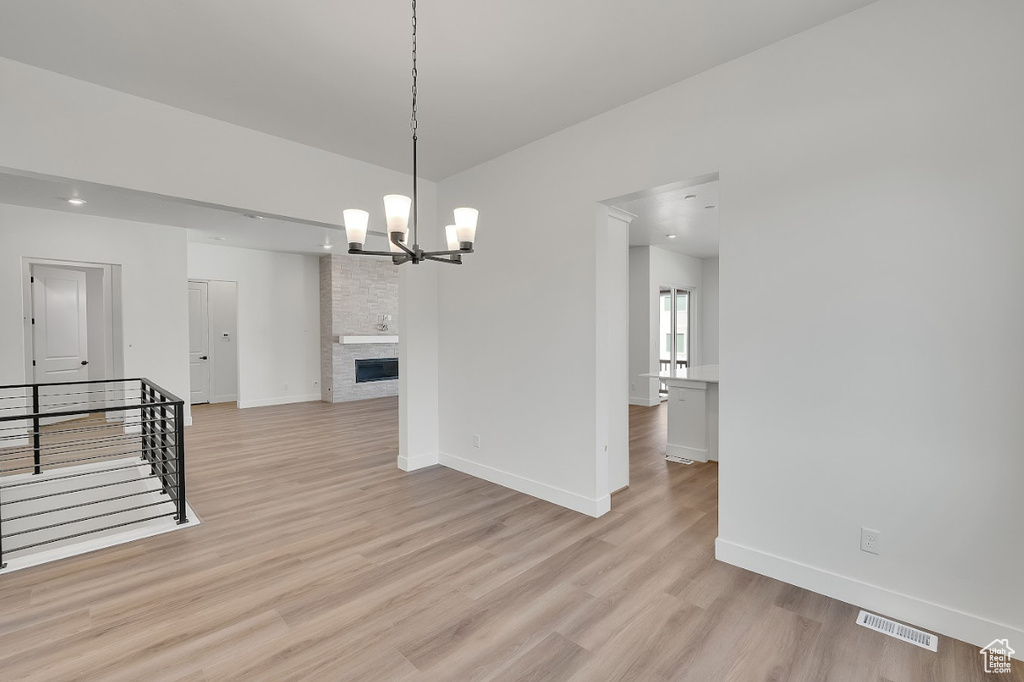 Unfurnished room with light wood-style flooring, a chandelier, recessed lighting, and a stone fireplace