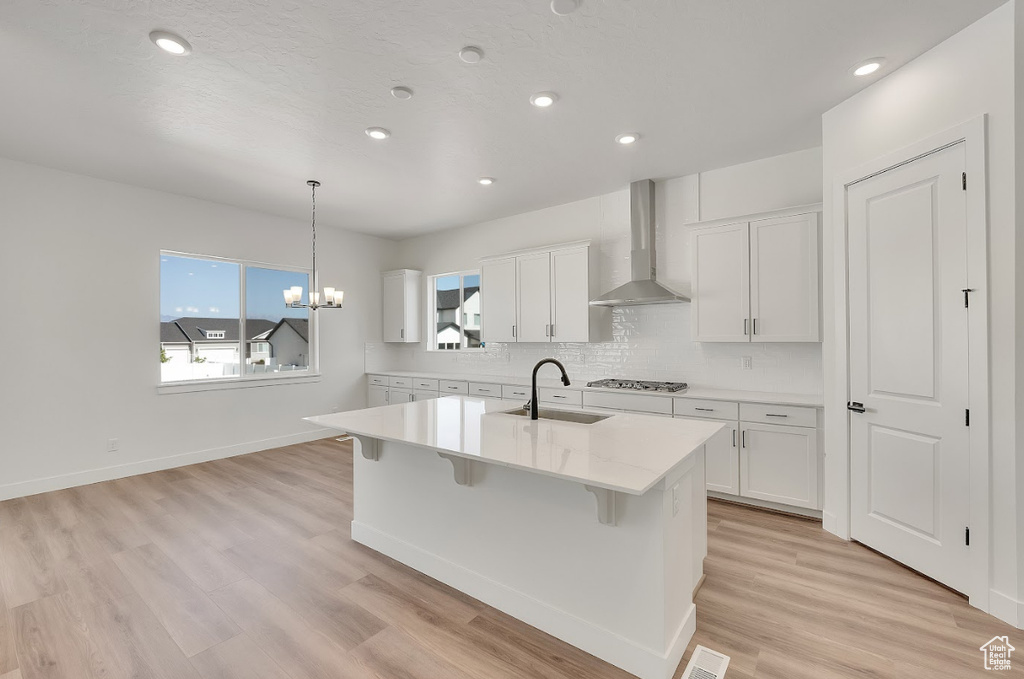 Kitchen with wall chimney range hood, gas cooktop, white cabinetry, decorative backsplash, and recessed lighting